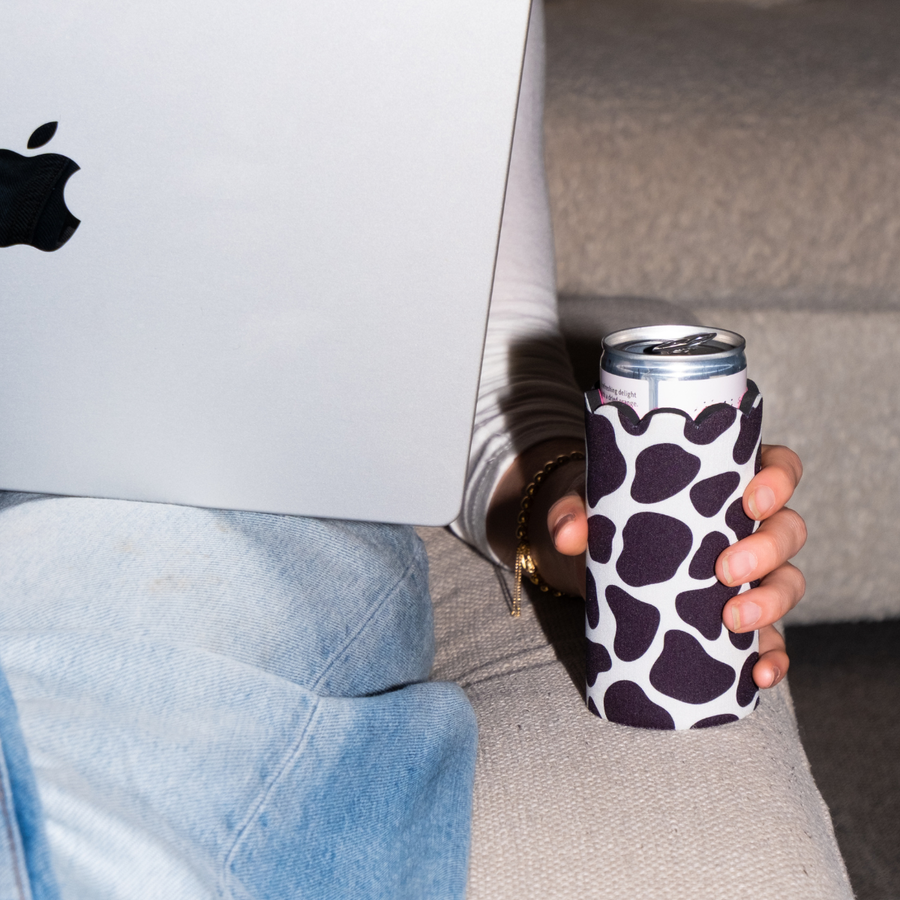 Person holding a Chic Sips scalloped can sleeve while using a laptop on a couch.