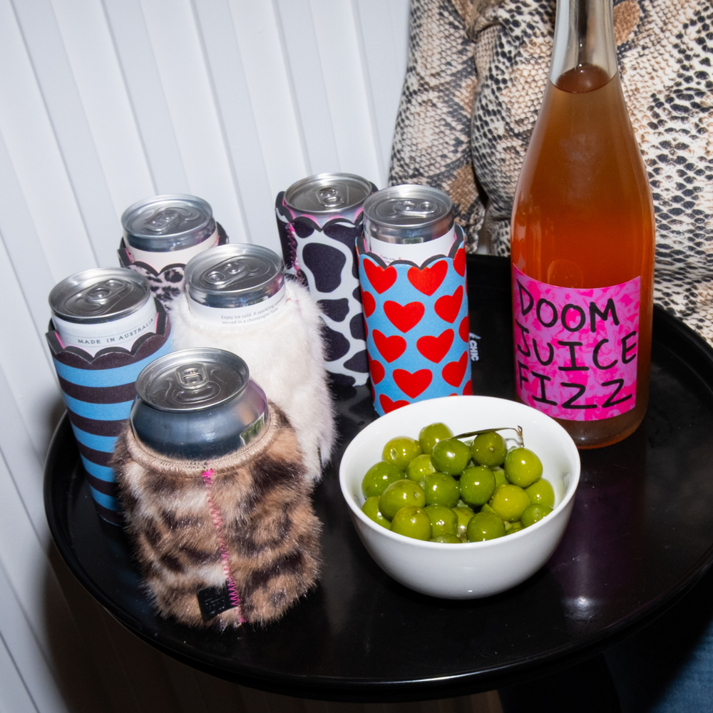 Assorted Chic Sips can sleeves displayed on a drinks tray with canned beverages, olives and a bottle of sparkling drink