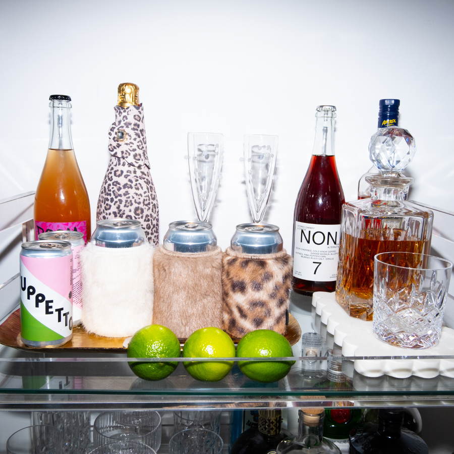 Faux fur Chic Sips can sleeves styled on a bar cart with canned drinks, champagne, glassware and spirits.