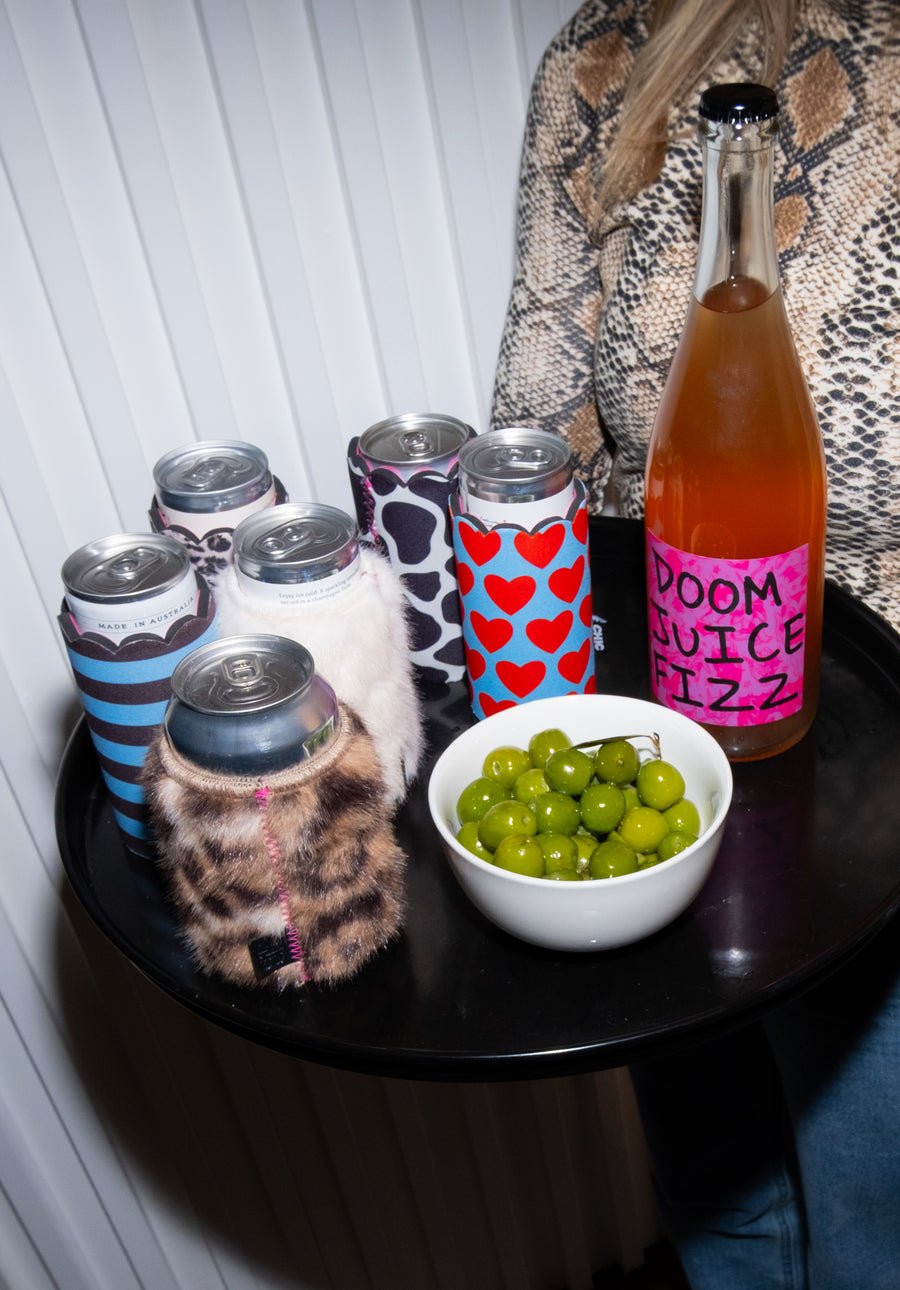 Assorted Chic Sips can sleeves displayed on a drinks tray with canned beverages, olives and a bottle of sparkling drink