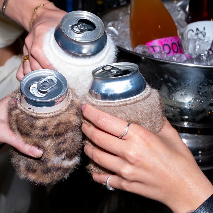 Three Chic Sips faux fur can sleeves in Priestess leopard, Uptown Brown and Monroe cream holding canned drinks beside an ice bucket
