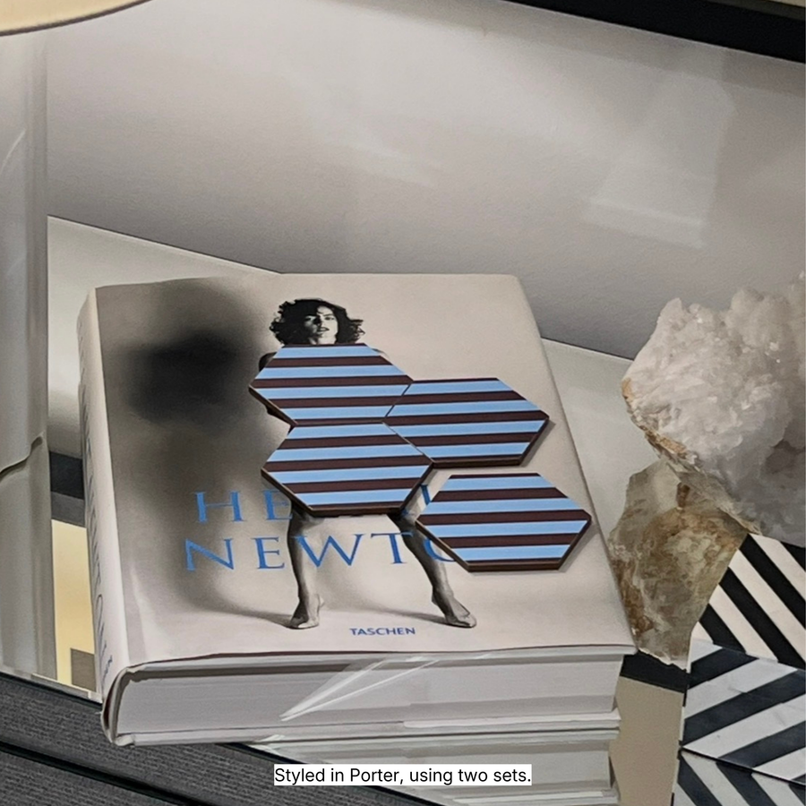 Hexagonal coasters in Porter blue and chocolate stripe pattern styled on a Helmut Newton book with decorative objects and a lamp