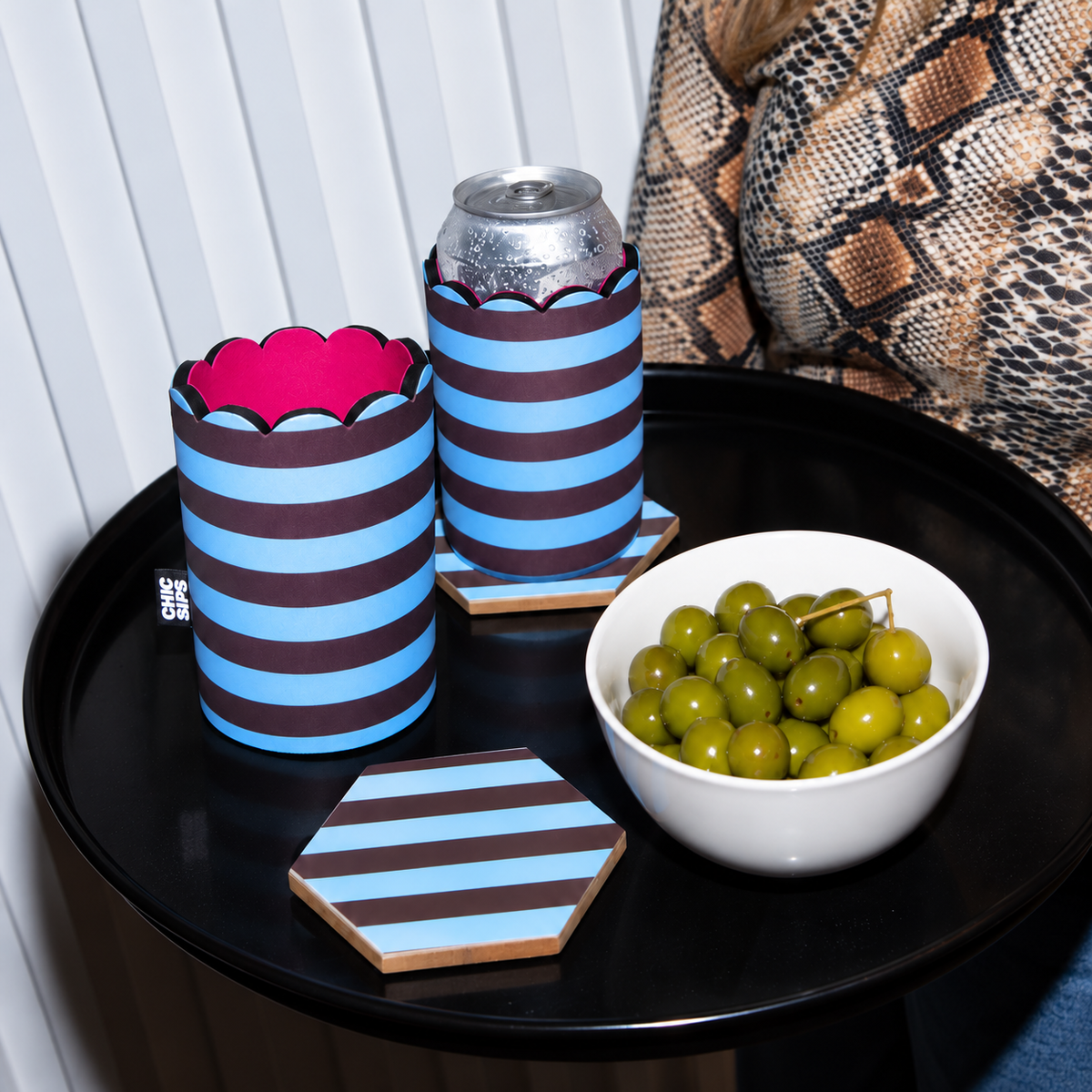 The Apéritif set in Porter blue and chocolate stripe print: can sleeves and coasters on a black side table with olives